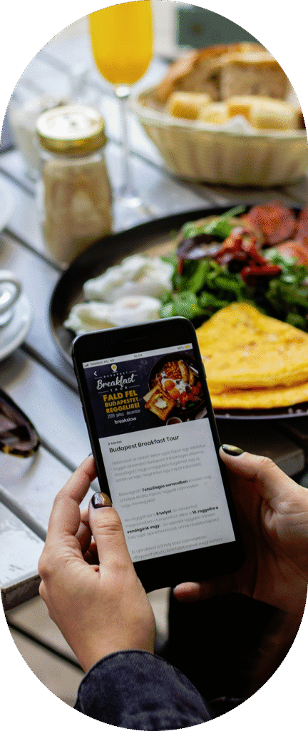 Osoba trzymająca telefon z otwartą stroną internetową restauracji. W tle widać stół na którym stoi jedzenie.