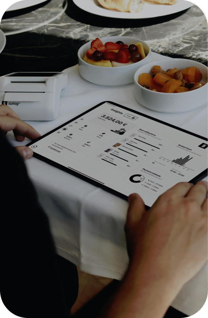 Tablet leżący na stole. Na jego ekranie widać panel analityczny. Na stole znajdują się miski z jedzeniem oraz kasa płatnicza.